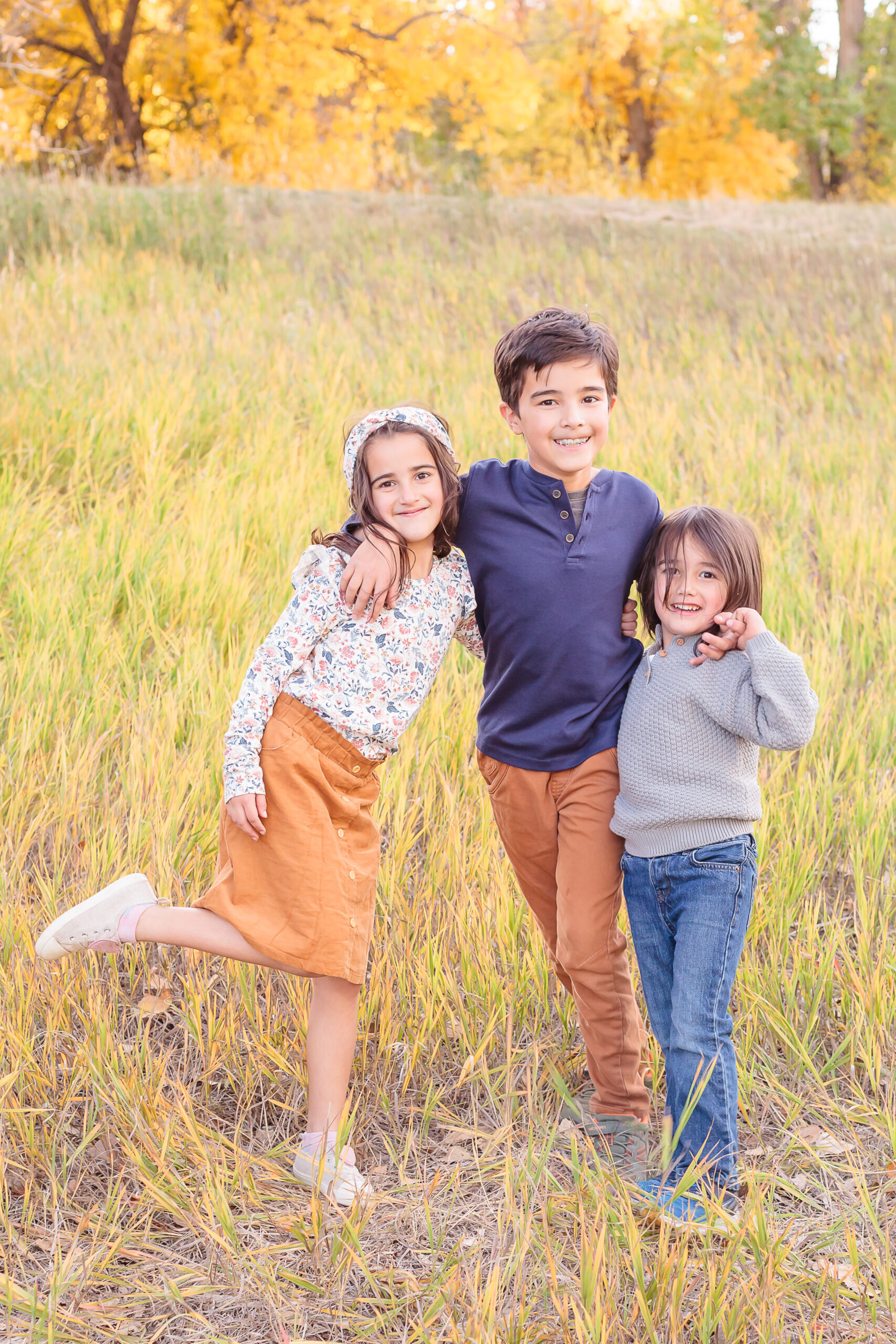 three young siblings with arms around each other, standing in tall yellow grass